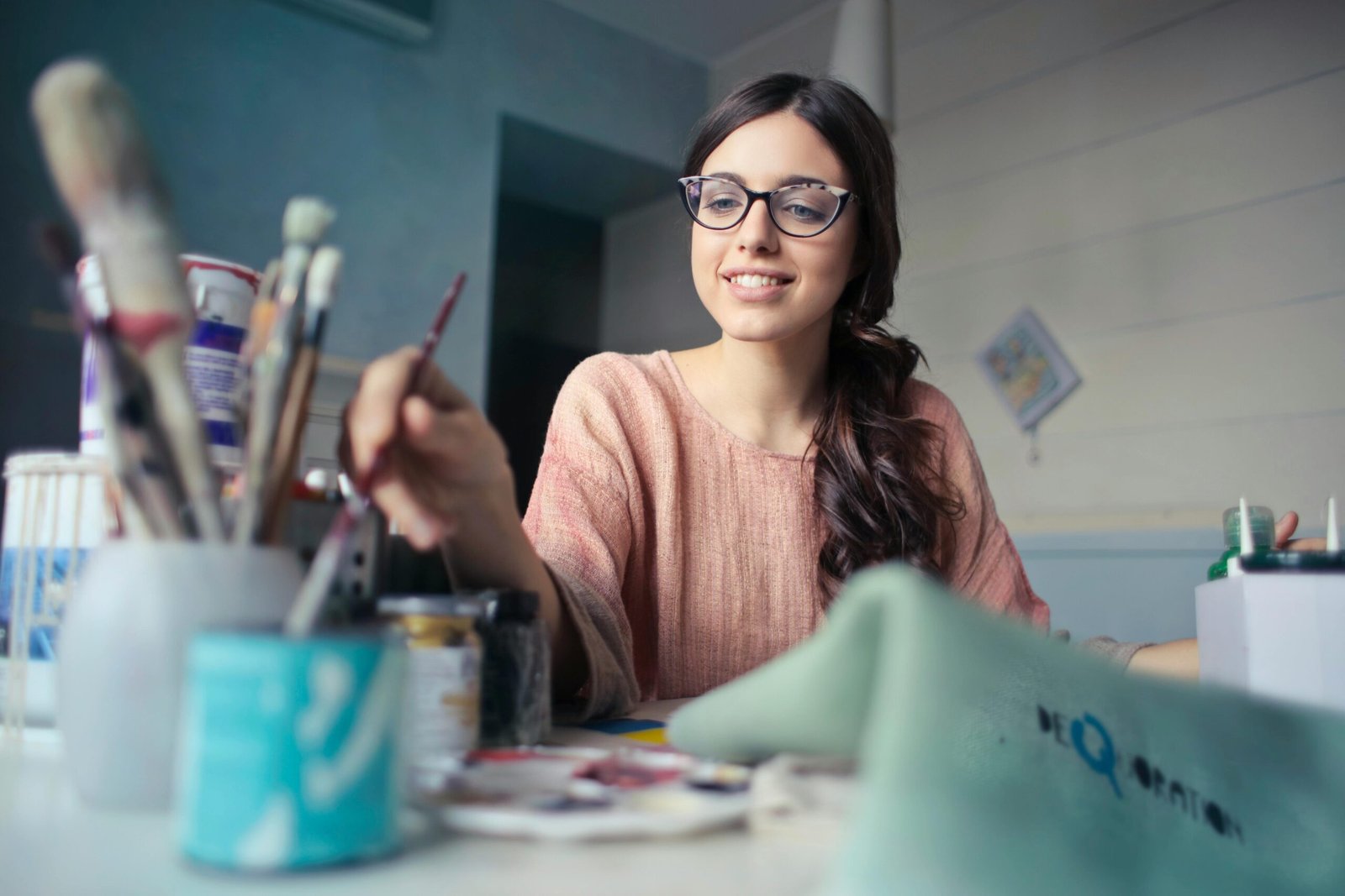A young woman artist working with paintbrushes in a creative studio setting.